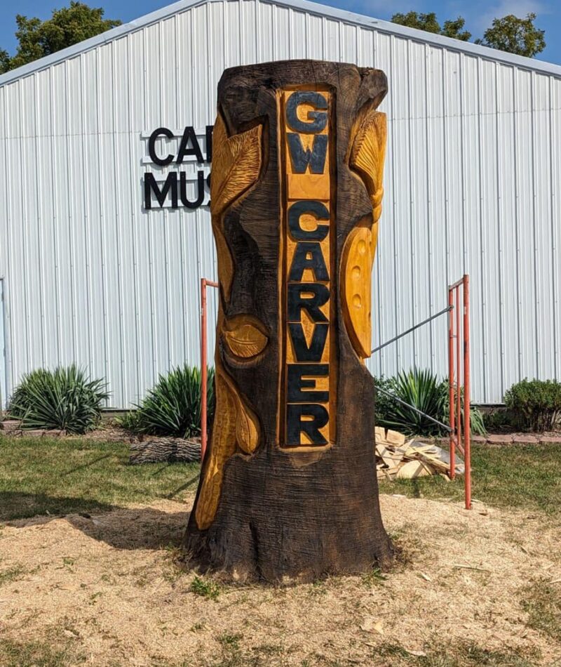 Wood carving of a tree trunk with the name G W CARVER and depictions of leaves and a peanut