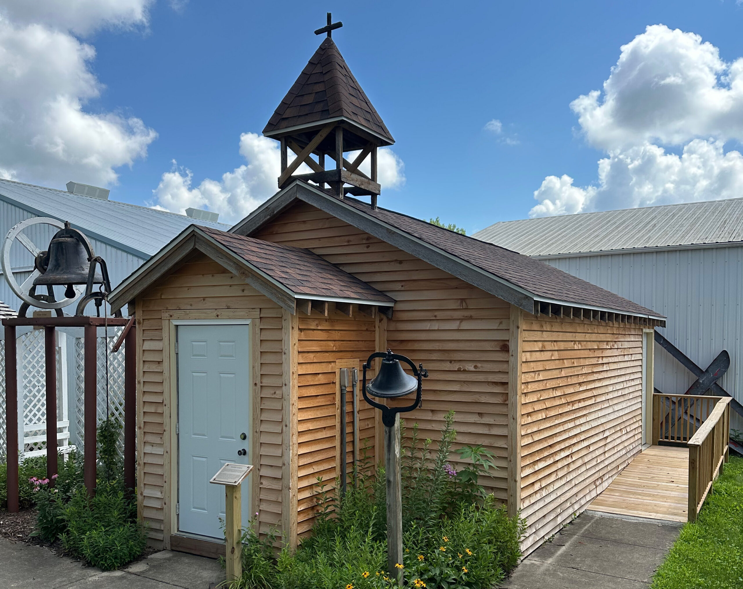 Heritage Village Church Small wooden chapel with a steeple and cross, with large bells on stands outside