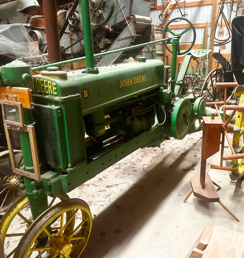 John Deere Tractor Machine Shed Vintage green and yellow John Deere Model B tractor with steel wheels in a barn full of antique farm equipment