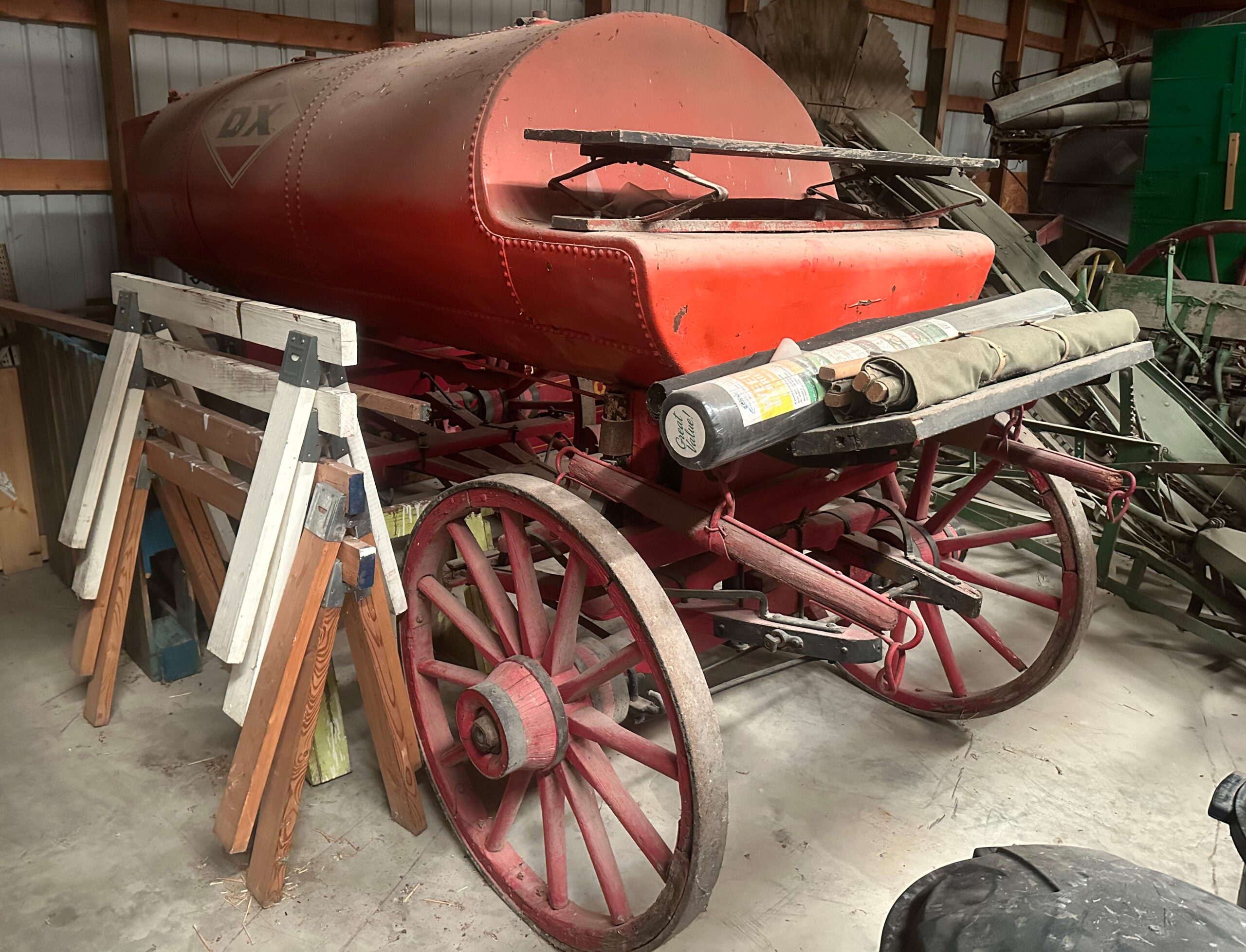 Machine Shed Vintage red horse-drawn tank wagon with wooden spoked wheels and a DX logo, stored in a shed