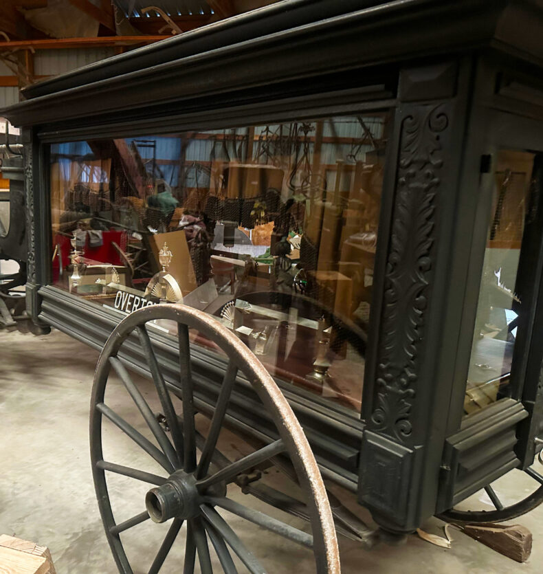 Overton Horse Drawn Herse Machine Shed Ornate black horse-drawn hearse with glass side panels and large wooden-spoked wheels