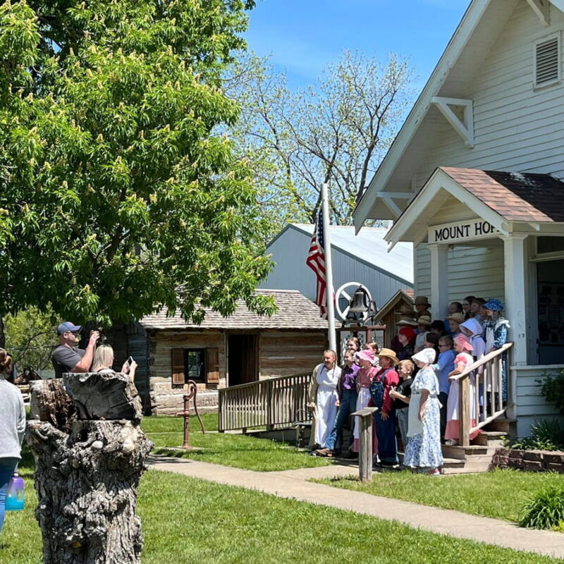 Children in 19th-century attire pose for a photo in front of the Mount Hope schoolhouse
