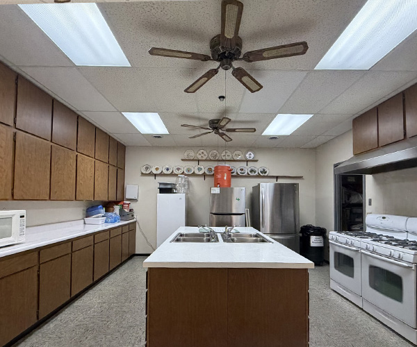 Large kitchen with wooden cabinets, a center island with a double sink, two refrigerators, and two white gas stoves