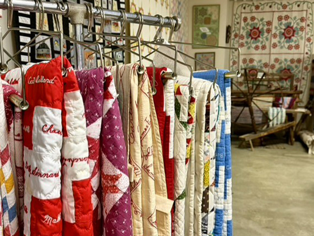 Handmade quilts with various patterns and signatures hanging on a metal display rack at Warren County Historical Society