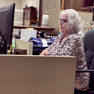 Older woman with white hair and glasses working at a computer in an office