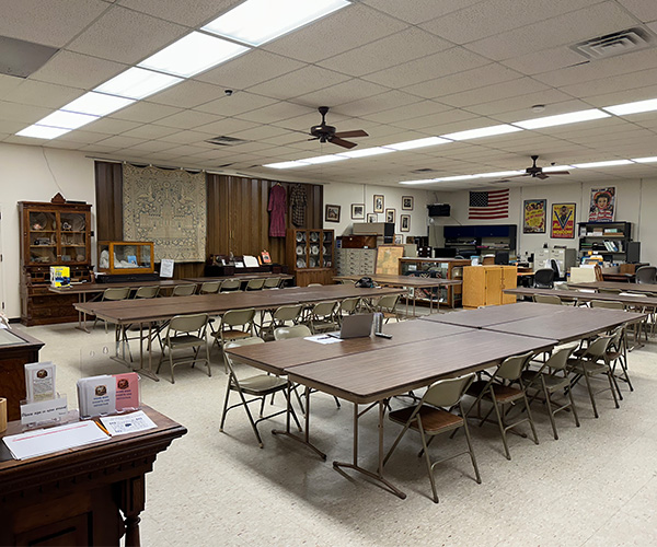 Meeting room with long folding tables, chairs, and walls decorated with historical artifacts, posters, and a flag